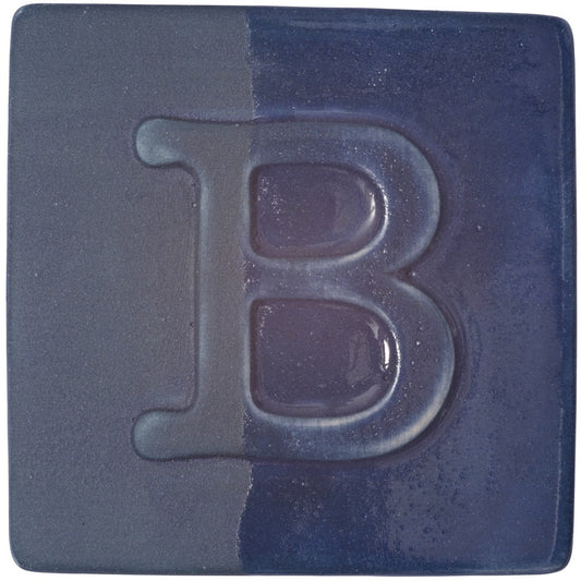 BOTZ engober. BOTZ:s provplatta med 9047 Dark Blue. Vänsterhalvan visar oglaserad engobe; högerhalvan visar samma engobe med ett tunt lager transparent glasyr.