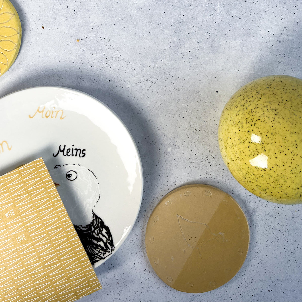 BOTZ engober. 9043 Gold Ochre på den ockrafärgade provplattan nere till höger. Vit lera, bränd vid 1050 °C. Övriga föremål visar andra färger.
